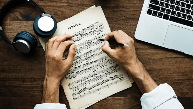 musician reading sheet music with laptop and headphones 
