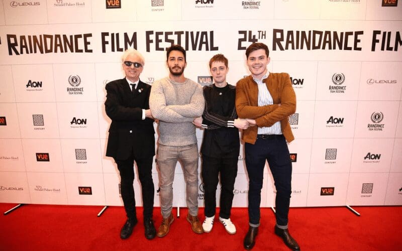 Elliot grove standing with 3 men in front of a Raindance film festival banner.