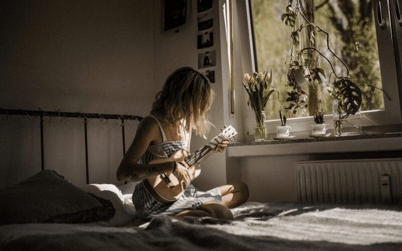girl playing guitar in bedroom with plants
