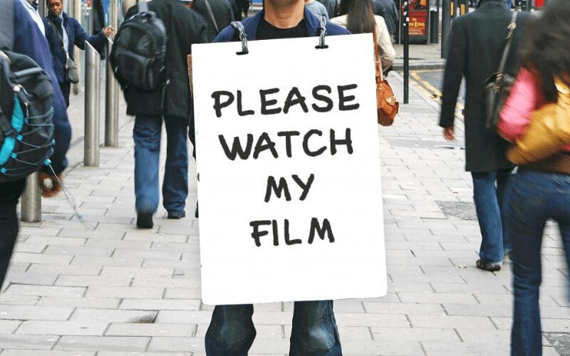 man holding a sign saying please watch my film 