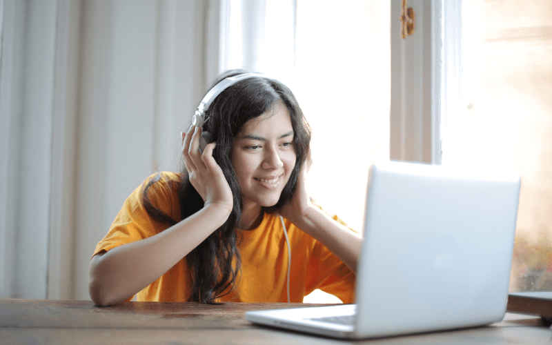 A woman wearing headphones.  She is listening to music sat at a laptop.