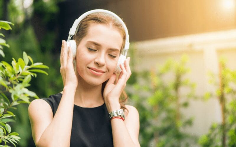 A woman who is outdoors, listening to music through white headphones.