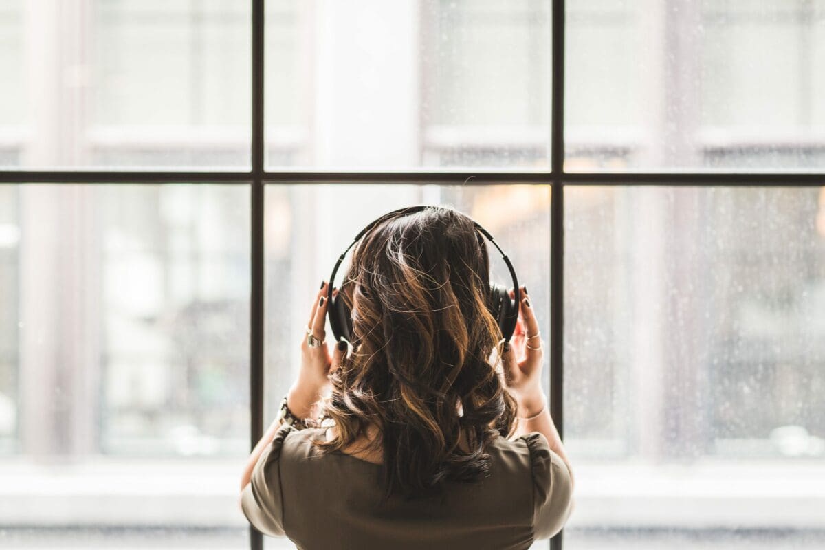 A woman with brown hair listening to music whilst looking through a window.